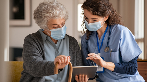 Alte Frau steht neben einer Krankenschwester und beide schauen auf ein Tablet