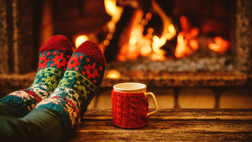 Zwei Füße mit Weihnachtssocken auf einem Tisch dahinter ein Kaminfeuer