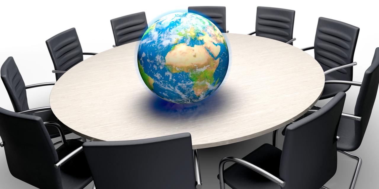 Ein runder Tisch mit leeren Stühlen drumherum und einer Weltkugel in der Mitte