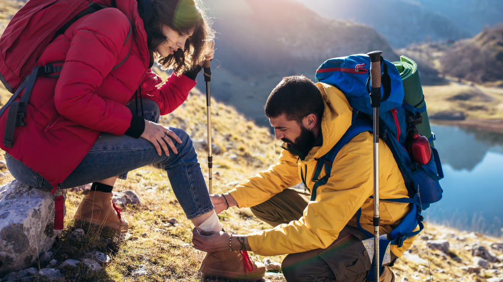 Eine Frau und ein Mann bei wandern in den Bergen, sie sitzt. Er kniet vor ihr und schaut nach ihrem Bein.