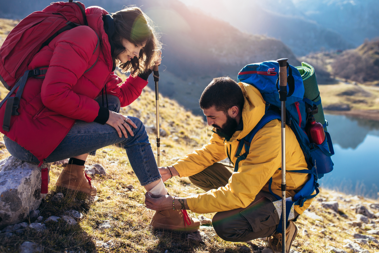 Eine Frau und ein Mann bei wandern in den Bergen, sie sitzt. Er kniet vor ihr und schaut nach ihrem Bein.