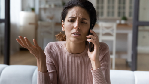 Frau telefoniert im Wohnzimmer, Gestik und Mimik wirken verärgert