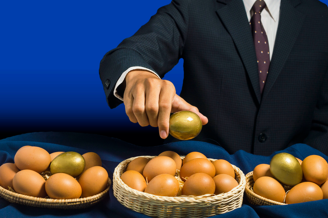 Mann mit Anzug legt goldene Eier in drei Körbe mit Eiern