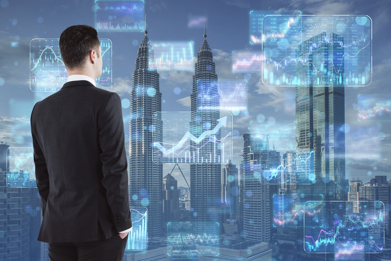 Stock market and investing concept with businessman back view looking at digital screens with financial chart diagrams, arrows and graphs on city skyscrapers background