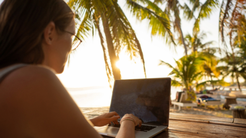 Eine Frau sitzt am Laptop und im Hintergrund Palmen und Sonne
