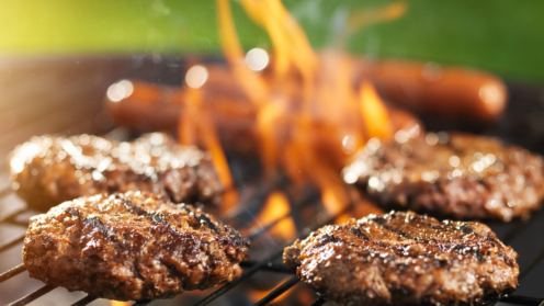 Hamburger und Hotdogs auf dem Grill, der Flammen wirft