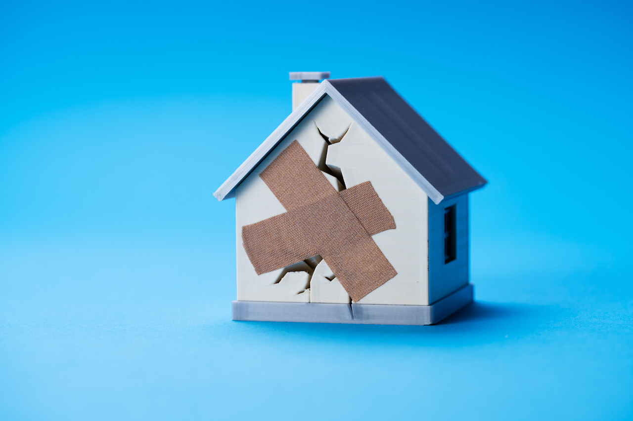 Model eines kaputten Hauses mit einem Riss und einem Pflaster darüber