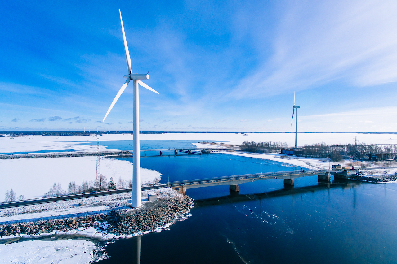 Luftaufnahme von Windmühlen mit blau gefrorenem Fluss im schneebedeckten Winter Finnland.