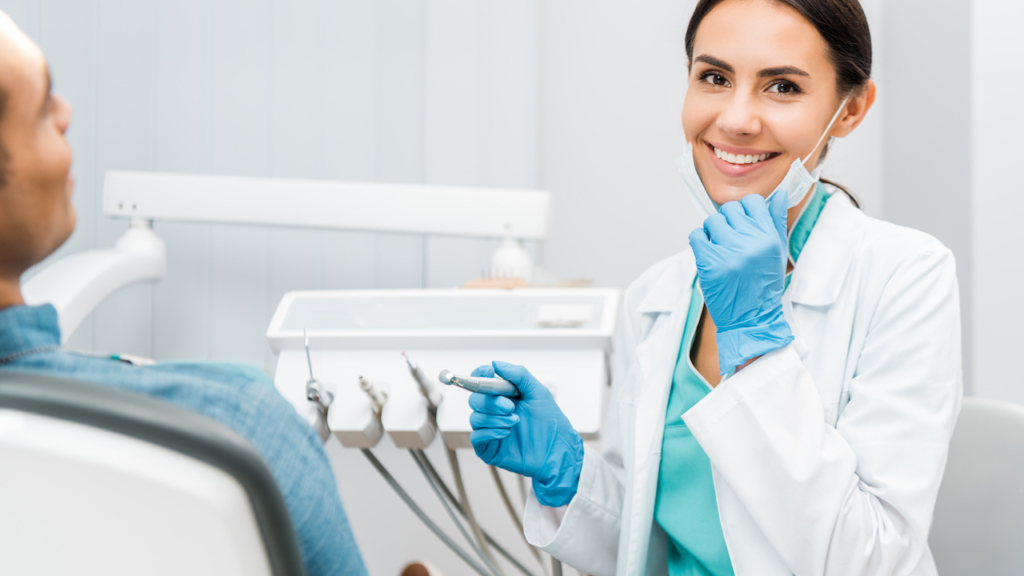 fröhliche Zahnärztin hält Bohrer in der Hand und lächelt neben Patientin