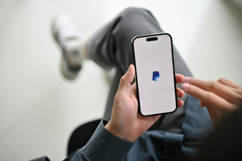 Nahaufnahme eines Mannes, der seine Rechnungen mit der mobilen PayPal-Anwendung bezahlt. iPhone mit PayPal Logo auf dem Bildschirm.