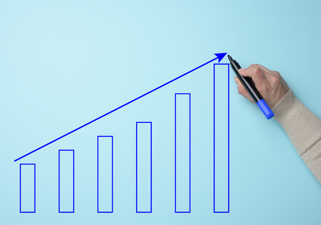 Graph with growing indicators and a female hand with a marker on a blue background. The concept of successful sales in business, inflation and rising prices