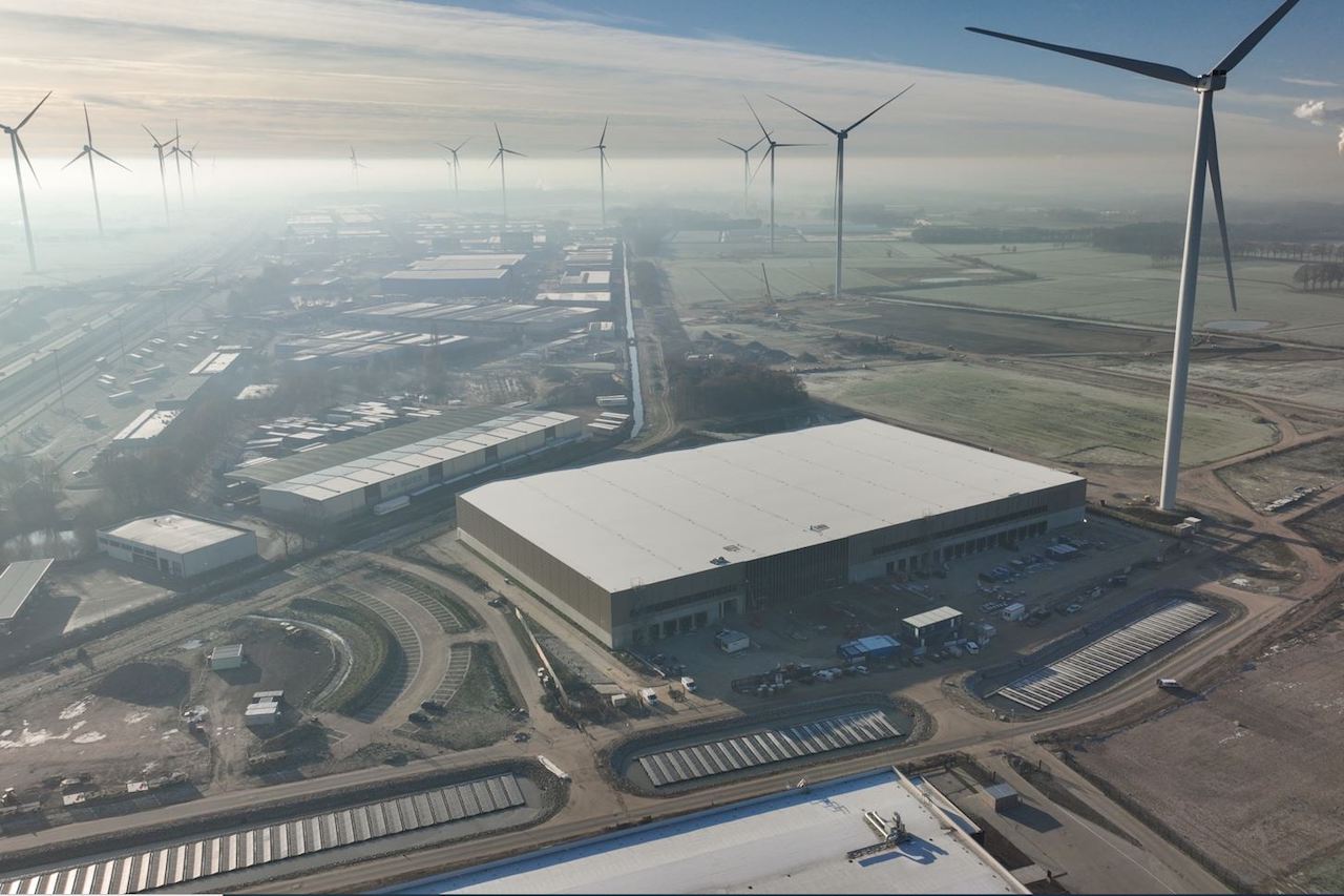 Luftaufnahme von Logistikhallen, umgeben von Windrädern
