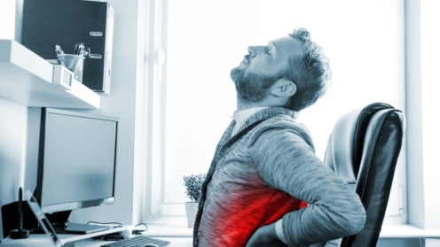Mann im Schreibtischbüro leidet unter Rückenschmerzen