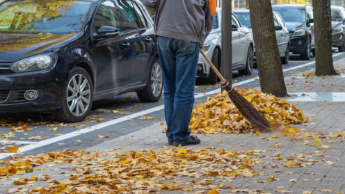 Ein Mitarbeiter der Stadt fegt im Herbst Laub vom Gehweg in einen Haufen.