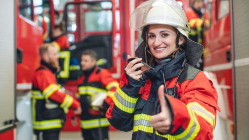 Feuerwehrfrau mit Helm in der Hand steht im Feuerwehrhaus