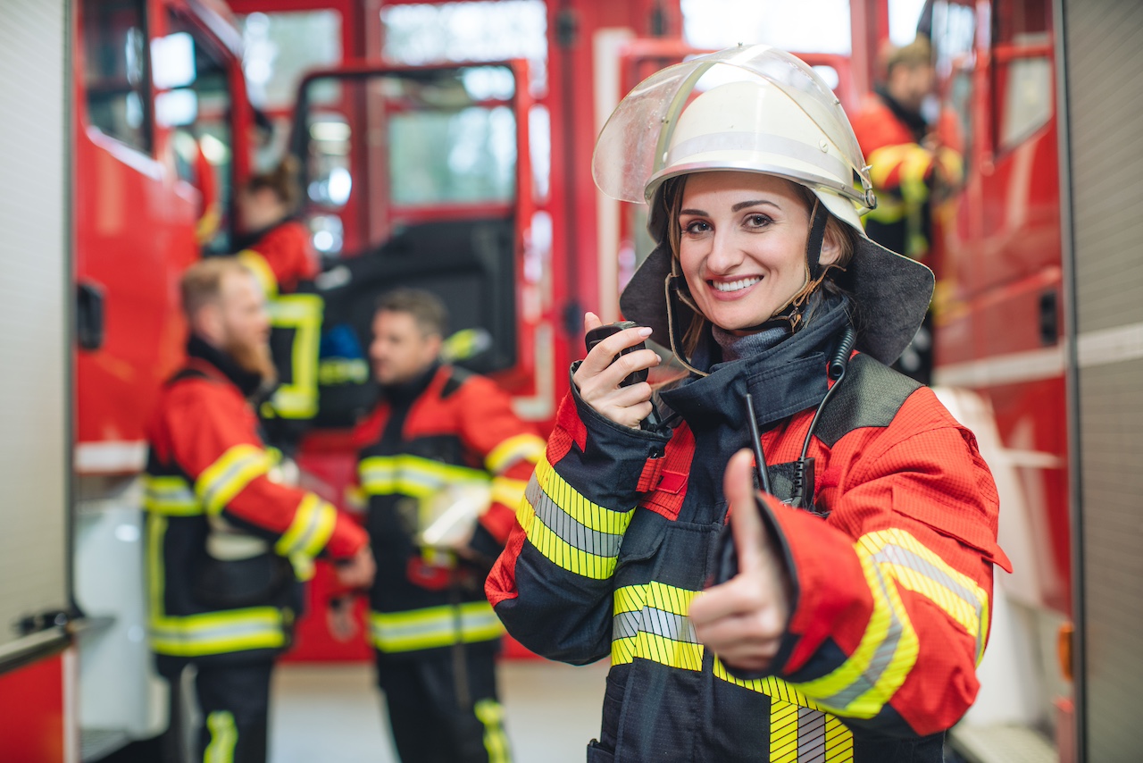 Feuerwehrfrau mit Helm in der Hand steht im Feuerwehrhaus