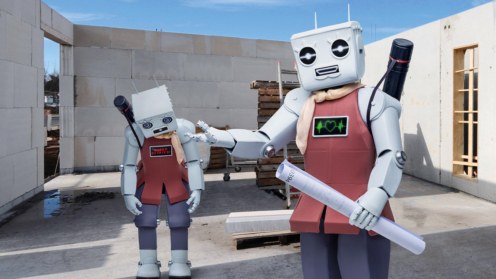 Zwei humanoide Roboter, die auf einer Baustelle stehen. Der eine Roboter ist außer Betrieb.