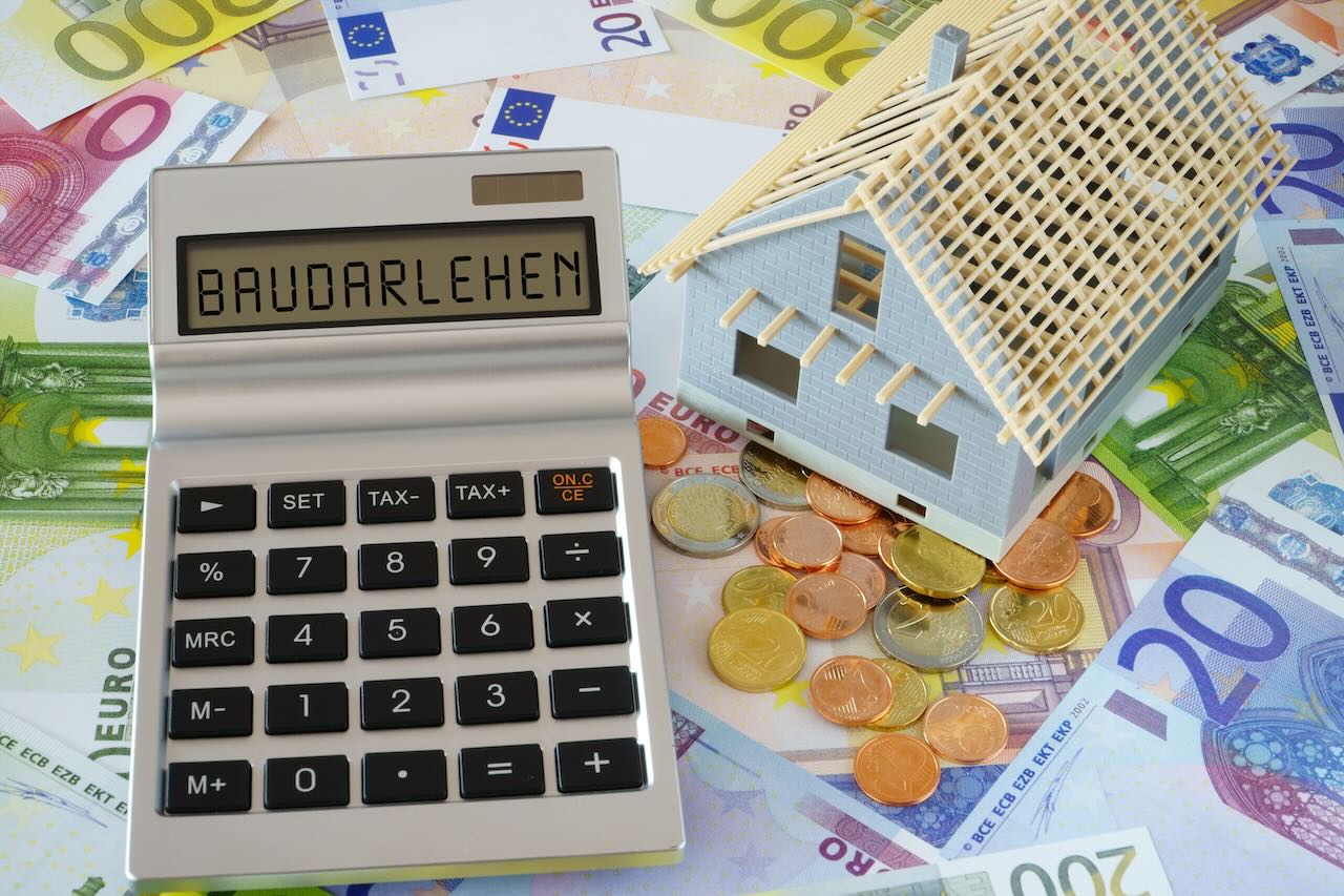Modellhaus und Taschenrechner mit dem Wort Baudarlehen auf dem Display auf Euro-Scheinen