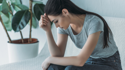 Frustrierte junge Frau in Depressionen sitzt auf Couch und schaut nach unten
