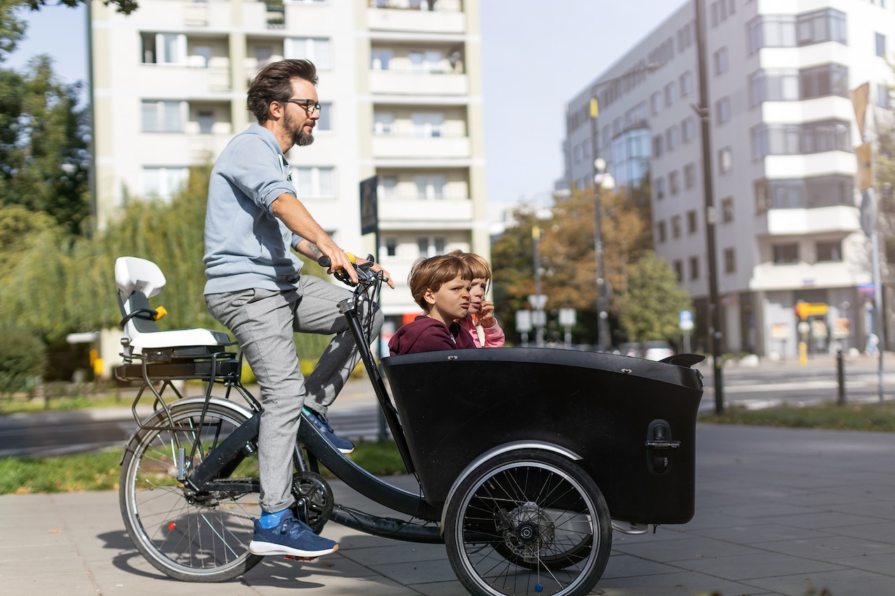Vater und Kinder bei einer Fahrt mit dem Lastenrad in einer Stadt