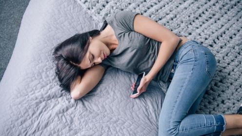 Ansicht einer traurigen, deprimierten Frau auf dem Bett mit Smartphone im Schlafzimme