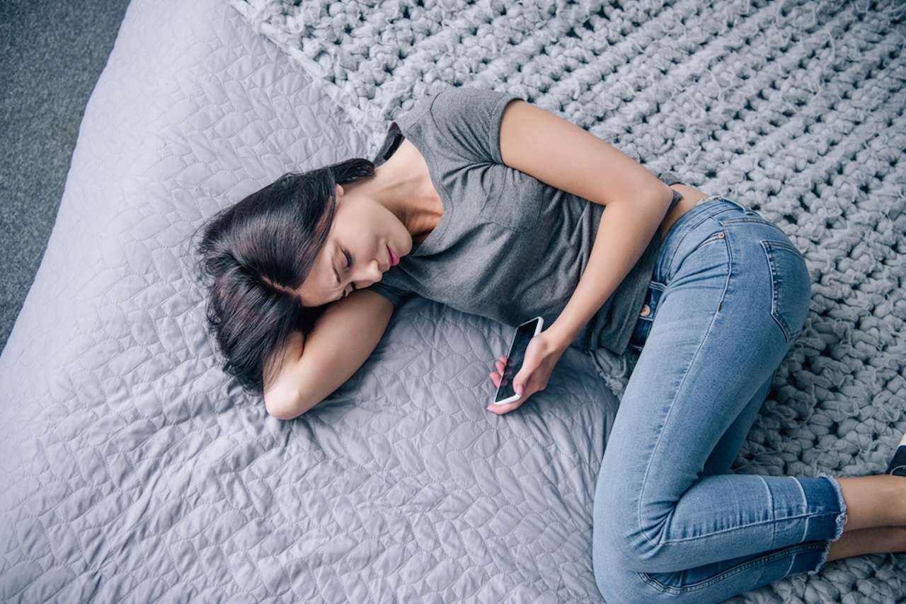 Ansicht einer traurigen, deprimierten Frau auf dem Bett mit Smartphone im Schlafzimme