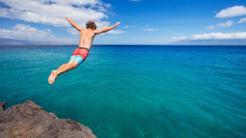 Mann springt von einer Klippe ins Meer. Sommer Spaß, Reise, Reiseschutz, Reiseschutzversicherung