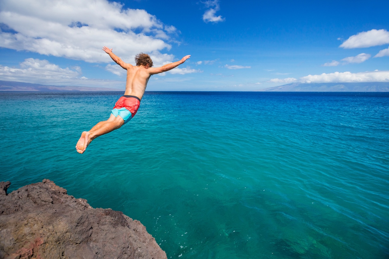 Mann springt von einer Klippe ins Meer. Sommer Spaß, Reise, Reiseschutz, Reiseschutzversicherung