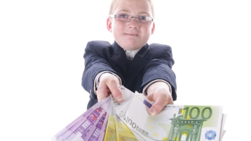 Kleiner Junge im dunklen Anzug spielt mit einem Bündel Geld, isoliert vor weißem Hintergrund.