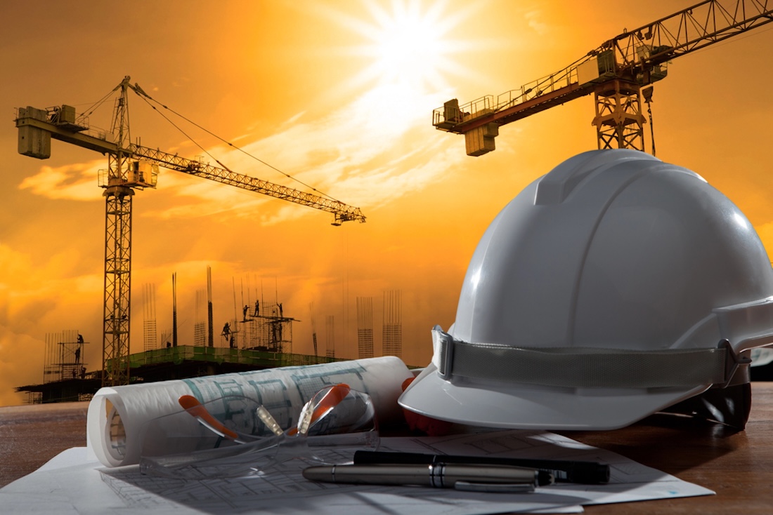 Schutzhelm und Architektenplan auf Holztisch mit Sonnenuntergangsszene