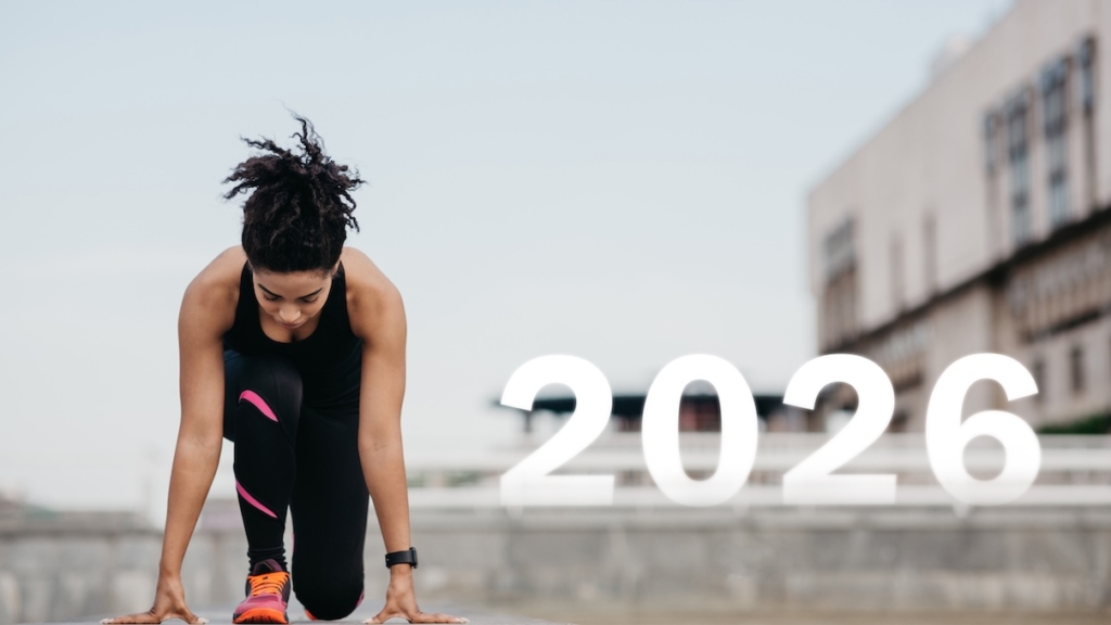 Eine Sportlerin in Trainingskleidung macht sich bereit, auf einer städtischen Laufbahn zu sprinten. Das Jahr 2026 ist deutlich zu sehen und symbolisiert ein bevorstehendes Ereignis. Neustart, Jahresbeginn 2026