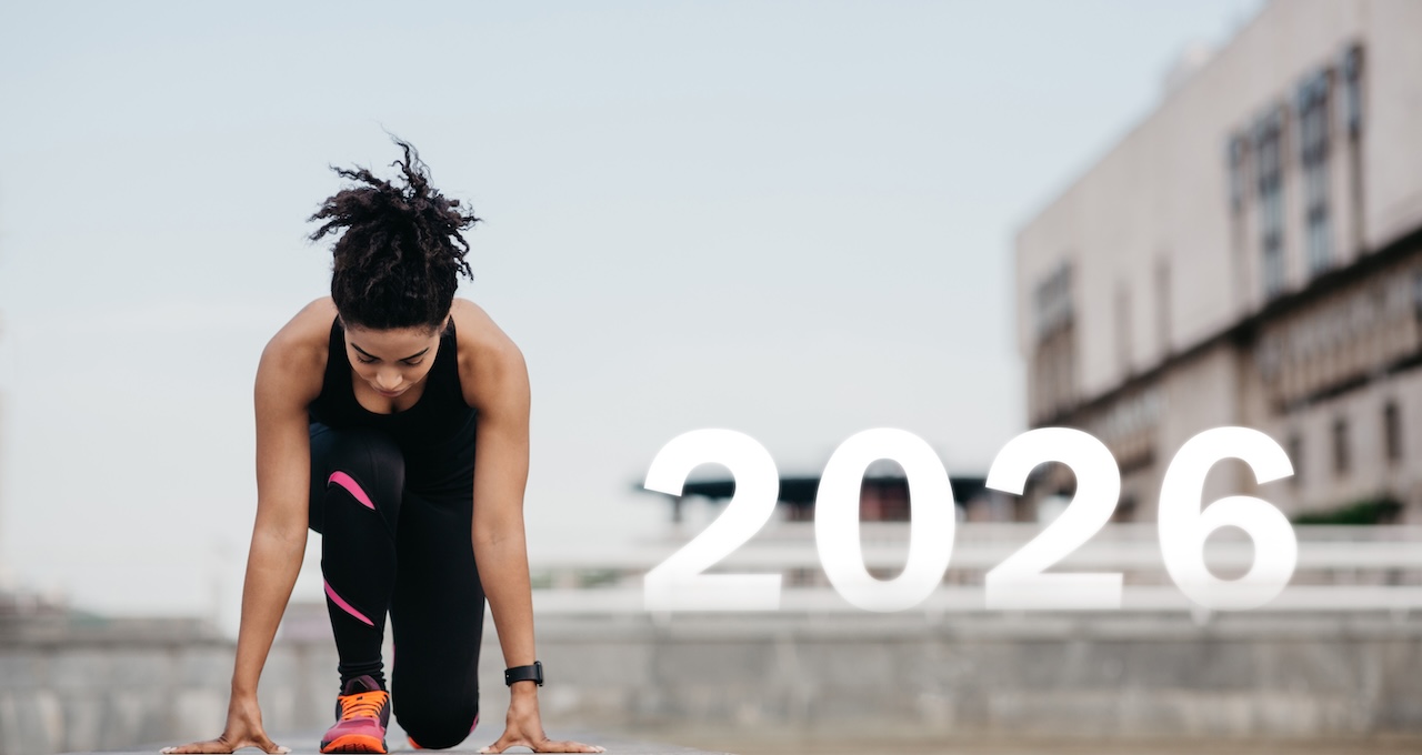 Eine Sportlerin in Trainingskleidung macht sich bereit, auf einer städtischen Laufbahn zu sprinten. Das Jahr 2026 ist deutlich zu sehen und symbolisiert ein bevorstehendes Ereignis. Neustart, Jahresbeginn 2026