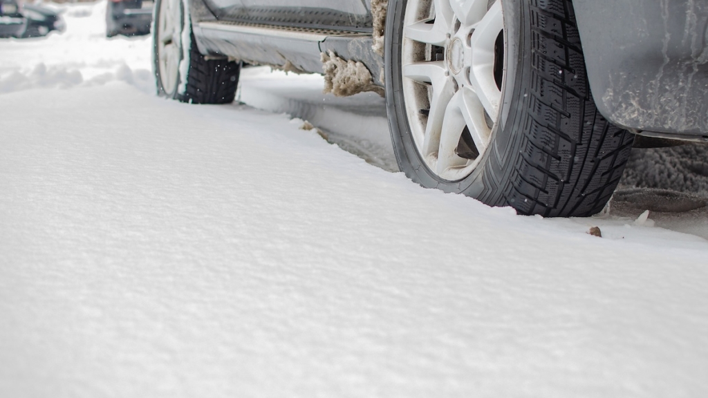 Nahaufnahme eines Autoreifens auf einer schneebedeckten Winterstraße. Auf dem Gummirad liegen Schneeflocken; Kfz; Kfz-Versicherung, Winter