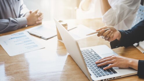 Kunden und Berater sitzen am Tisch, man sieht einen Laptop und schriftliche Unterlagen.