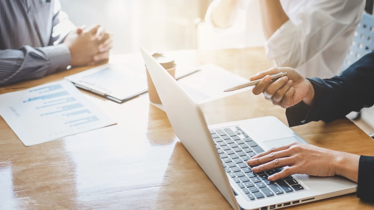Kunden und Berater sitzen am Tisch, man sieht einen Laptop und schriftliche Unterlagen.