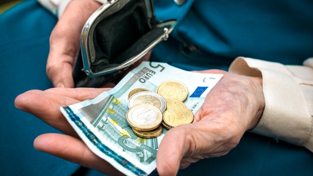 Euroschein und Münzen in der Hand eines Rentners.