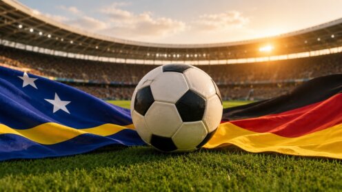 Fußball liegt zwischen der Flagge Curaçaos und der Deutschlandflagge in einem sonnigen Stadion.