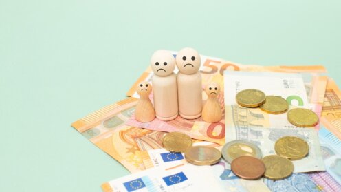 Münzen, Geldbörse, Holzfiguren und Sparschwein mit Schirm als Symbol für Einkommen und Vorsorge.
