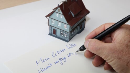Modellhaus auf einem Blatt Papier, auf dem jemand seinen letzten Willen schreibt
