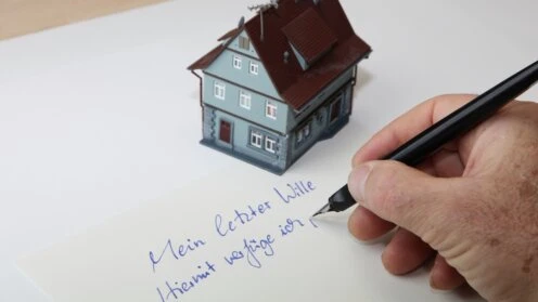 Modellhaus auf einem Blatt Papier, auf dem jemand seinen letzten Willen schreibt