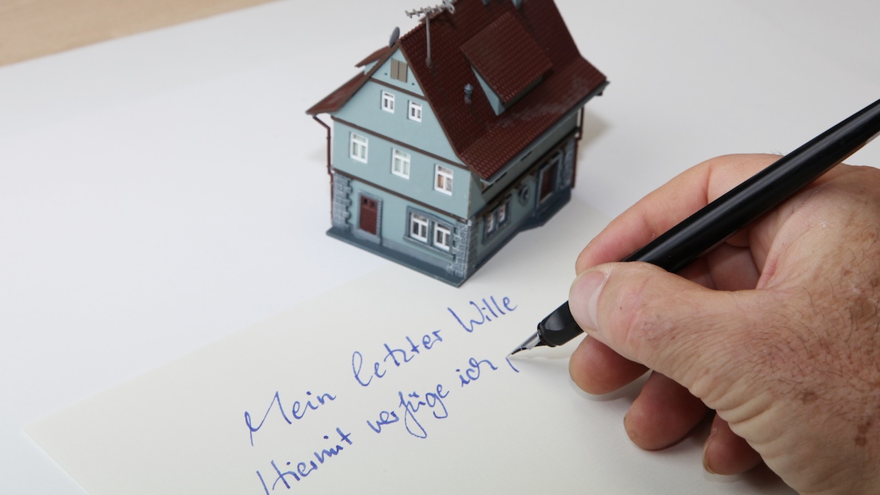 Modellhaus auf einem Blatt Papier, auf dem jemand seinen letzten Willen schreibt