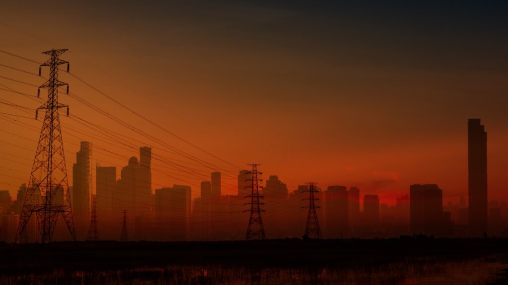 Hochspannungsleitungen vor der Silhouette einer Großstadt in der Abenddämmerung.