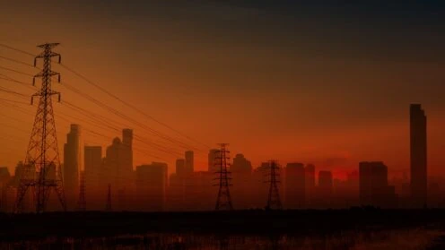 Hochspannungsleitungen vor der Silhouette einer Großstadt in der Abenddämmerung.