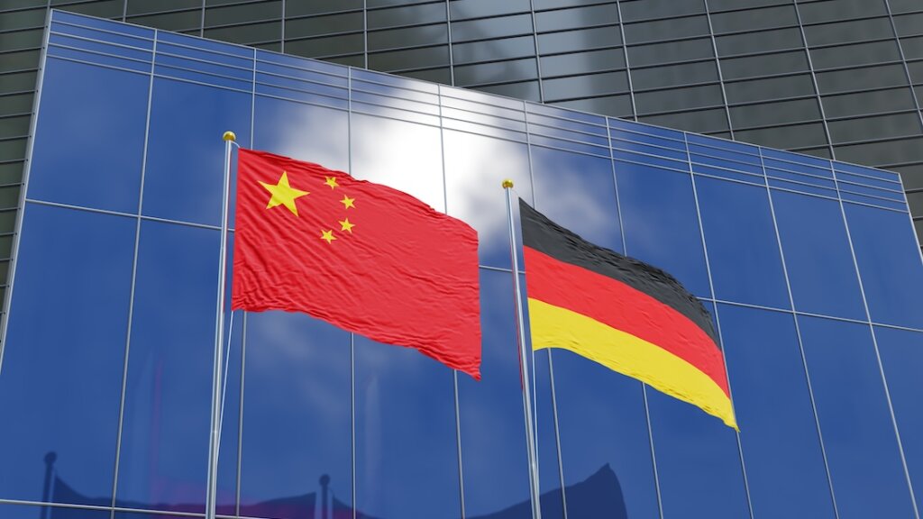 Flaggen Chinas und Deutschlands vor den Fassaden moderner Geschäftsgebäude.