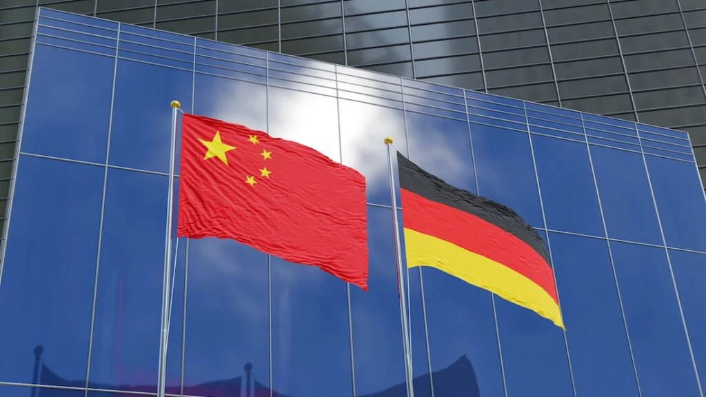 Flaggen Chinas und Deutschlands vor den Fassaden moderner Geschäftsgebäude.