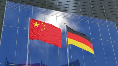 Flaggen Chinas und Deutschlands vor den Fassaden moderner Geschäftsgebäude.