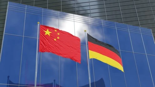 Flaggen Chinas und Deutschlands vor den Fassaden moderner Geschäftsgebäude.