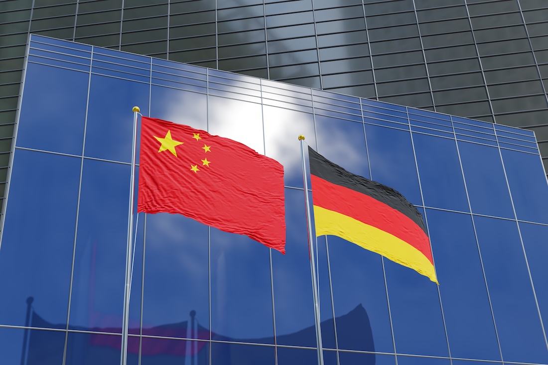 Flaggen Chinas und Deutschlands vor den Fassaden moderner Geschäftsgebäude.