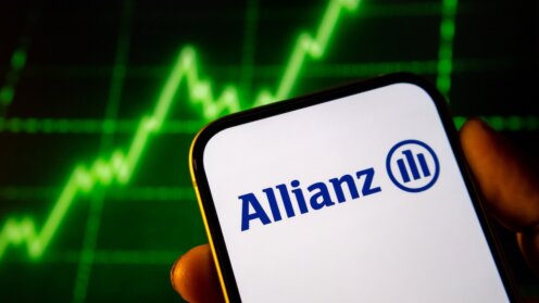 Smartphone mit Allianz-Logo auf dem Display vor einem Bildschirm mit einem Börsenkurs.