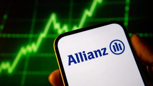 Smartphone mit Allianz-Logo auf dem Display vor einem Bildschirm mit einem Börsenkurs.